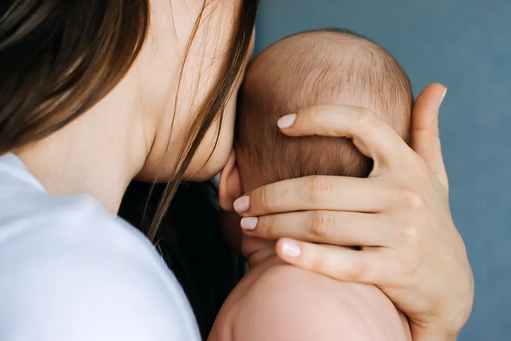Mother holding and gently cradling a newborn baby close to her shoulder