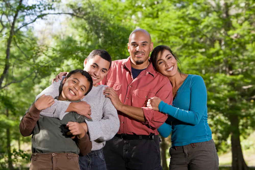 Smiling family of four standing together outdoors with arms around each other