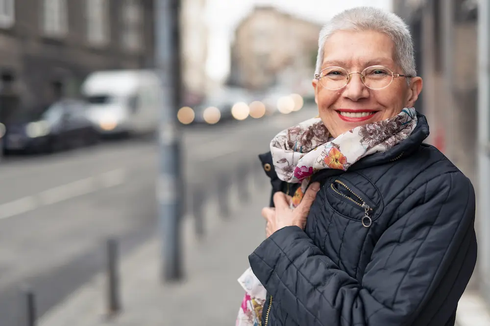Smiling older woman wearing glasses and a scarf standing on a city street
