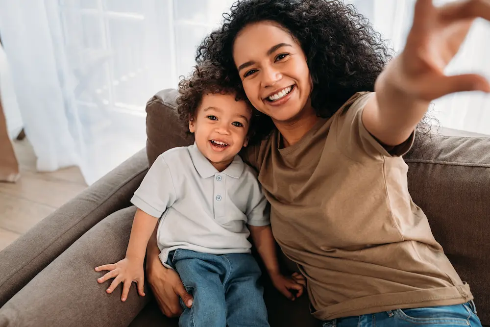 Woman and young boy sitting together on a couch smiling while taking a selfie