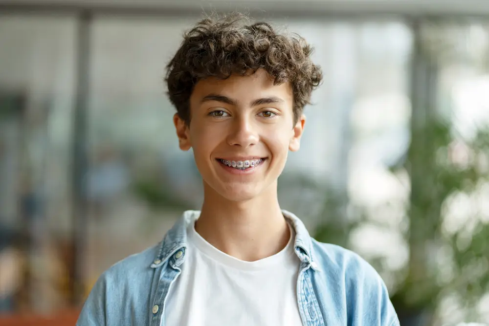 Smiling teenage boy with curly hair wearing braces and casual clothing